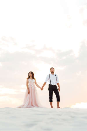 young couple a guy in black breeches and a girl in a pink dress are walking along the white sand of the desertの写真素材
