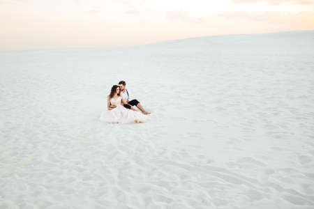 young couple a guy in black breeches and a girl in a pink dress are walking along the white sand of the desertの写真素材