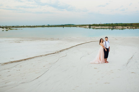young couple a guy in black breeches and a girl in a pink dress are walking along the white sand of the desertの写真素材