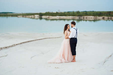 young couple a guy in black breeches and a girl in a pink dress are walking along the white sand of the desertの写真素材