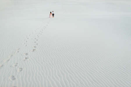 young couple a guy in black breeches and a girl in a pink dress are walking along the white sand of the desertの写真素材