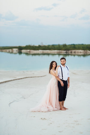 young couple a guy in black breeches and a girl in a pink dress are walking along the white sand of the desertの写真素材