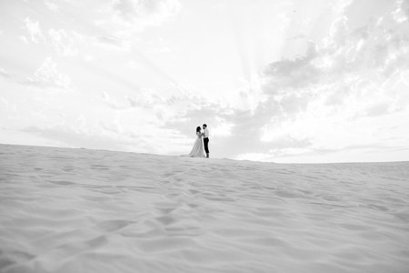 young couple a guy in black breeches and a girl in a pink dress are walking along the white sand of the desertの写真素材