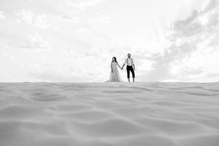 young couple a guy in black breeches and a girl in a pink dress are walking along the white sand of the desertの写真素材