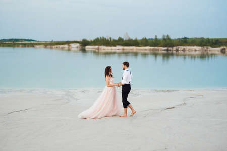 young couple a guy in black breeches and a girl in a pink dress are walking along the white sand of the desertの写真素材