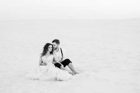 young couple a guy in black breeches and a girl in a pink dress are walking along the white sand of the desertの写真素材