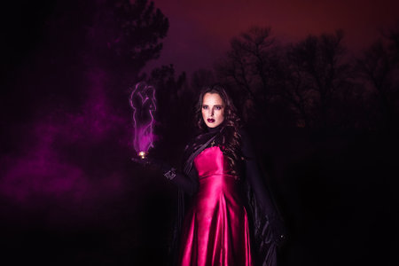 girl alone at night in the forest brews a potion and wonders for marriage, surrounded by candles and smokeの写真素材