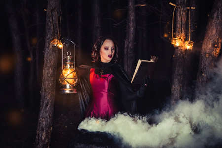 girl alone at night in the forest brews a potion and wonders for marriage, surrounded by candles and smokeの写真素材