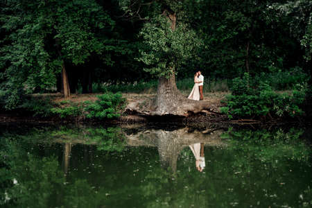 a guy and a girl are walking along the banks of a wild river overgrown with willows and forestの写真素材