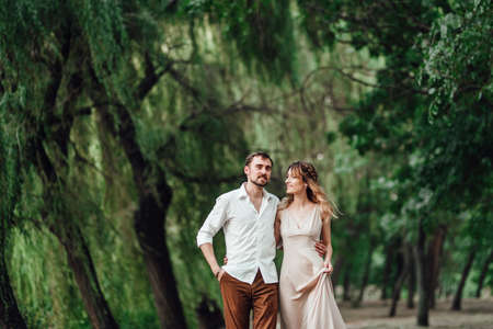 a guy and a girl are walking along the banks of a wild river overgrown with willows and forestの写真素材