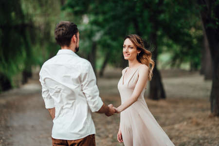 a guy and a girl are walking along the banks of a wild river overgrown with willows and forestの写真素材