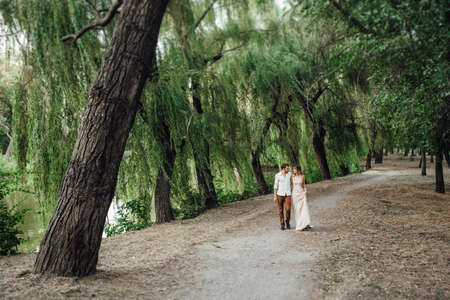 a guy and a girl are walking along the banks of a wild river overgrown with willows and forestの写真素材