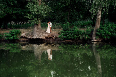 a guy and a girl are walking along the banks of a wild river overgrown with willows and forestの写真素材