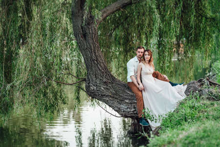 a guy and a girl are sitting together on a crooked tree on the steep bank of a wild riverの写真素材