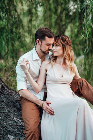 a guy and a girl are sitting together on a crooked tree on the steep bank of a wild riverの写真素材
