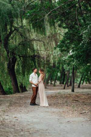 a guy and a girl are walking along the banks of a wild river overgrown with willows and forestの写真素材