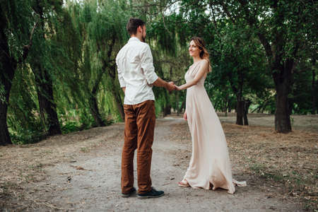 a guy and a girl are walking along the banks of a wild river overgrown with willows and forestの写真素材