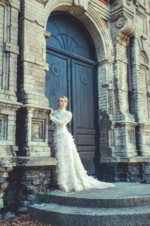 Blonde girl in a retro dress on the background of the old dark door of the buildingの写真素材