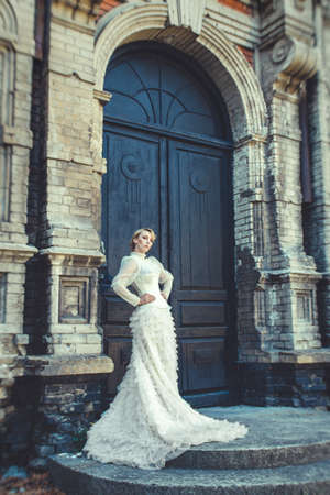 Blonde girl in a retro dress on the background of the old dark door of the buildingの写真素材
