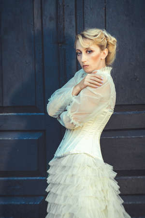 Blonde girl in a retro dress on the background of the old dark door of the buildingの写真素材