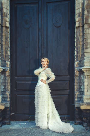 Blonde girl in a retro dress on the background of the old dark door of the buildingの写真素材