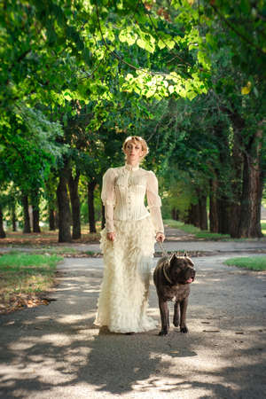 Girl in an old dress with ruffles and a big dark dogの写真素材