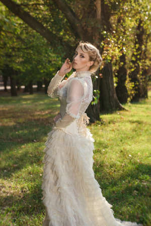 Girl model with white hair in a retro dress with ruffles in a green parkの写真素材