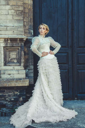 Blonde girl in a retro dress on the background of the old dark door of the buildingの写真素材