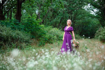 Girl model blonde in a lilac dress with a bouquet with a green forestの写真素材