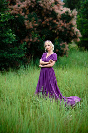 Girl model blonde in a lilac dress with a bouquet with a green forestの写真素材