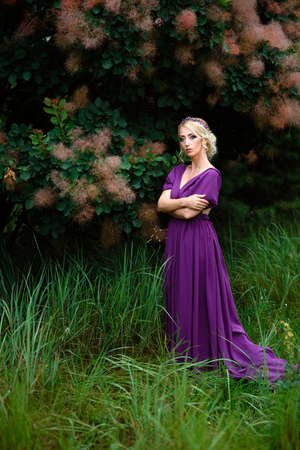 Girl model blonde in a lilac dress with a bouquet with a green forestの写真素材