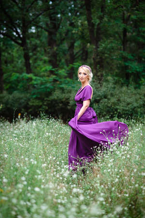 Girl model blonde in a lilac dress with a bouquet with a green forestの写真素材