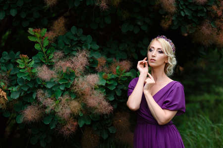 Girl model blonde in a lilac dress with a bouquet with a green forestの写真素材