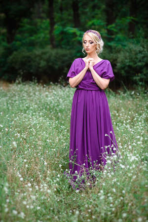 Girl model blonde in a lilac dress with a bouquet with a green forestの写真素材