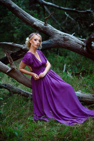 Girl model blonde in a lilac dress with a bouquet with a green forestの写真素材