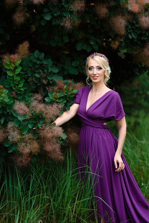 Girl model blonde in a lilac dress with a bouquet with a green forestの写真素材