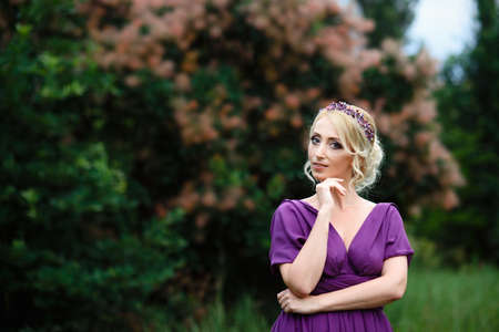 Girl model blonde in a lilac dress with a bouquet with a green forestの写真素材