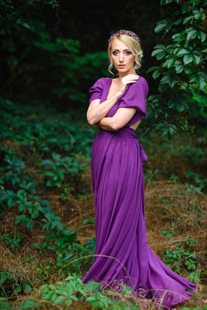 Girl model blonde in a lilac dress with a bouquet with a green forestの写真素材