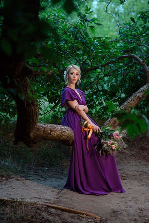 Girl model blonde in a lilac dress with a bouquet with a green forestの写真素材