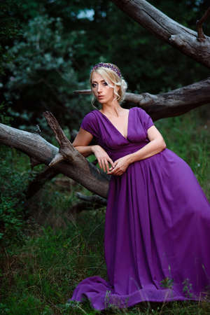 Girl model blonde in a lilac dress with a bouquet with a green forestの写真素材
