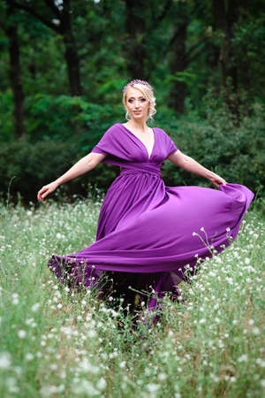 Girl model blonde in a lilac dress with a bouquet with a green forestの写真素材