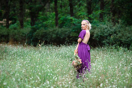 Girl model blonde in a lilac dress with a bouquet with a green forestの写真素材