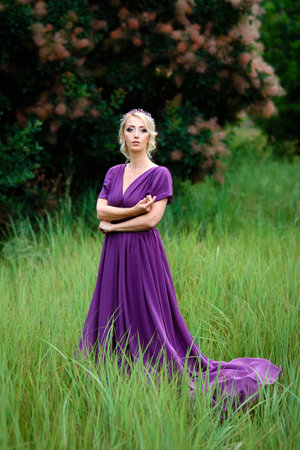 Girl model blonde in a lilac dress with a bouquet with a green forestの写真素材