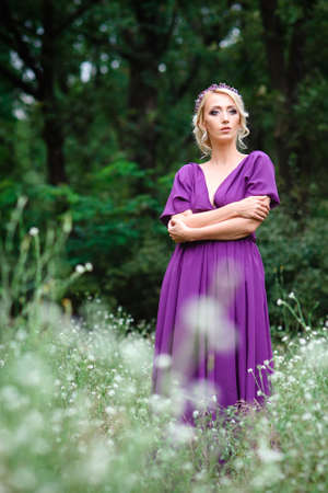 Girl model blonde in a lilac dress with a bouquet with a green forestの写真素材