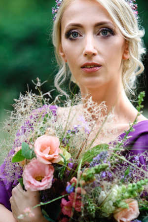 Girl model blonde in a lilac dress with a bouquet with a green forestの写真素材