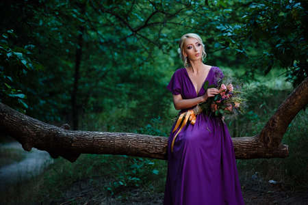 Girl model blonde in a lilac dress with a bouquet with a green forestの写真素材