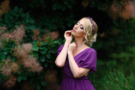 Girl model blonde in a lilac dress with a bouquet with a green forestの写真素材