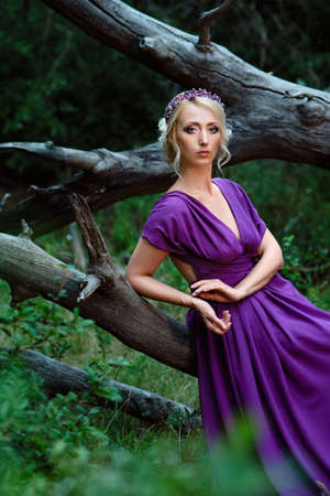 Girl model blonde in a lilac dress with a bouquet with a green forestの写真素材