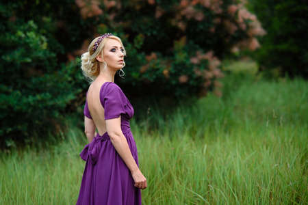 Girl model blonde in a lilac dress with a bouquet with a green forestの写真素材