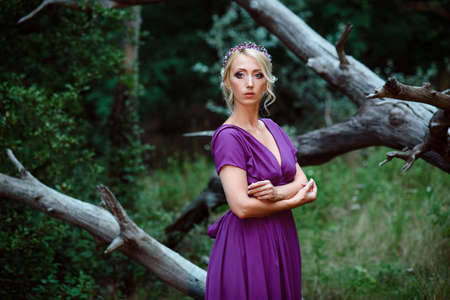 Girl model blonde in a lilac dress with a bouquet with a green forestの写真素材